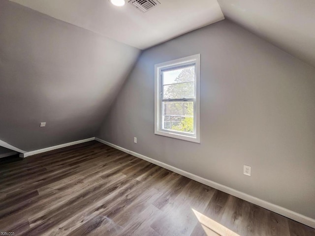 additional living space featuring visible vents, baseboards, vaulted ceiling, and dark wood-style floors