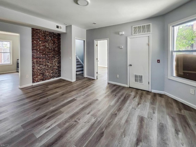 unfurnished living room featuring visible vents, stairs, plenty of natural light, and wood finished floors