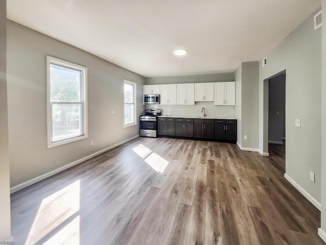 kitchen featuring appliances with stainless steel finishes, a sink, light wood finished floors, white cabinetry, and baseboards