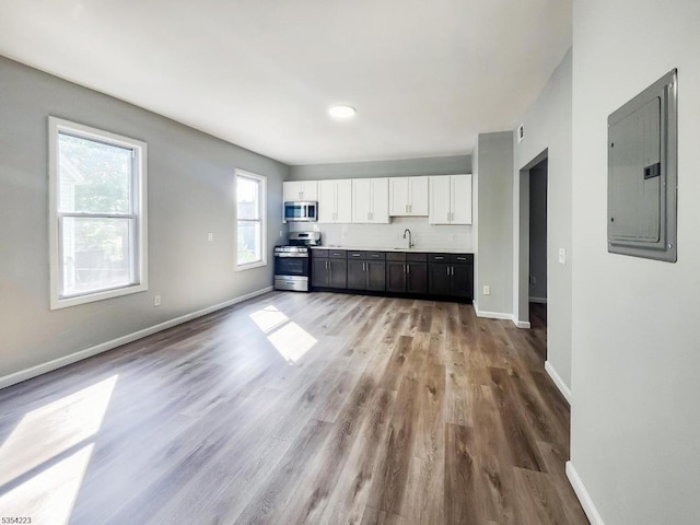 unfurnished living room featuring light wood-style floors, baseboards, electric panel, and a sink