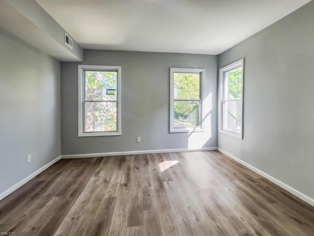 empty room featuring visible vents, plenty of natural light, and wood finished floors