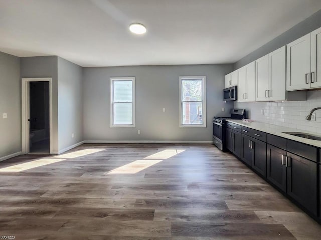 kitchen with decorative backsplash, baseboards, white cabinets, a sink, and appliances with stainless steel finishes