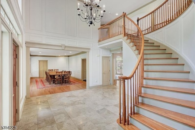 staircase featuring an inviting chandelier, ornamental molding, a decorative wall, and a towering ceiling