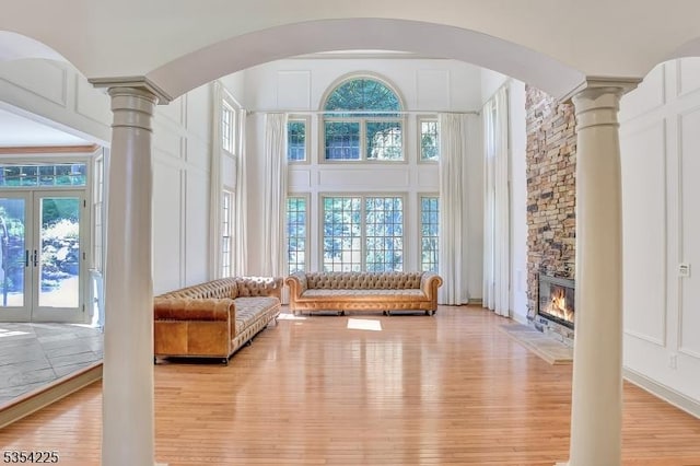 interior space with arched walkways, decorative columns, a stone fireplace, and light wood-type flooring