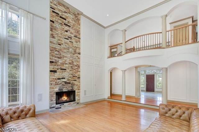 unfurnished living room featuring light wood-style floors, arched walkways, a high ceiling, and decorative columns
