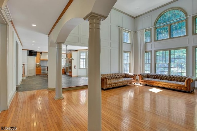 interior space featuring decorative columns, arched walkways, light wood finished floors, ornamental molding, and a decorative wall