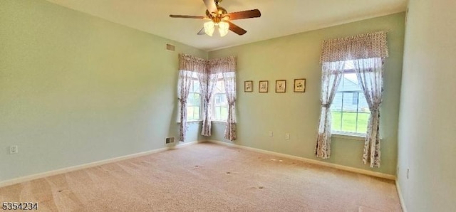 carpeted empty room featuring a ceiling fan, baseboards, visible vents, and plenty of natural light