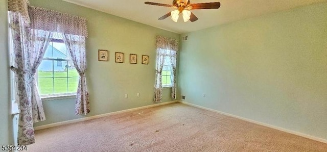 carpeted spare room featuring a healthy amount of sunlight, baseboards, a ceiling fan, and visible vents