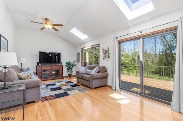 living area featuring a ceiling fan, baseboards, vaulted ceiling with skylight, and hardwood / wood-style floors