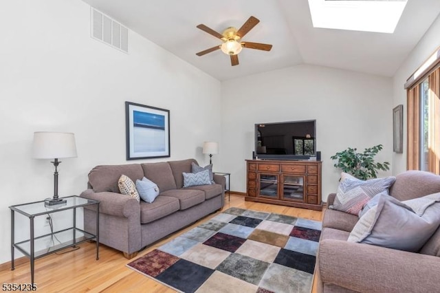 living room with vaulted ceiling with skylight, ceiling fan, wood finished floors, and visible vents