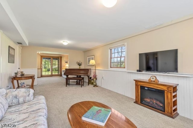 carpeted living area featuring a healthy amount of sunlight, wainscoting, a glass covered fireplace, and visible vents