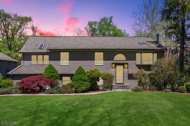 bi-level home with a shingled roof, a chimney, and a front lawn
