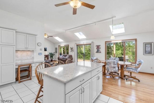 kitchen featuring hanging light fixtures, vaulted ceiling with skylight, a ceiling fan, tasteful backsplash, and a kitchen island