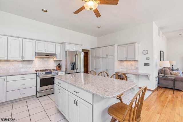 kitchen with a breakfast bar, stainless steel appliances, a ceiling fan, decorative backsplash, and under cabinet range hood