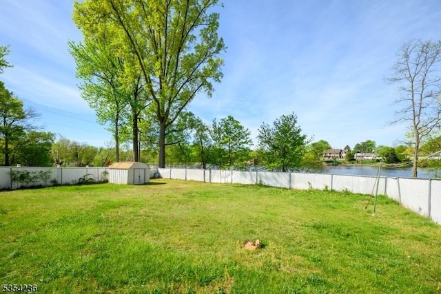 view of yard featuring an outdoor structure, a water view, a fenced backyard, and a storage unit