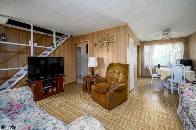living area featuring ceiling fan, wood walls, and stairway