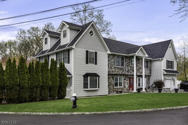 view of front of property with stone siding, a front yard, and roof with shingles