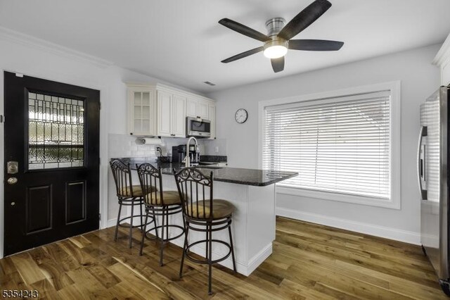 kitchen featuring appliances with stainless steel finishes, baseboards, white cabinets, a peninsula, and glass insert cabinets