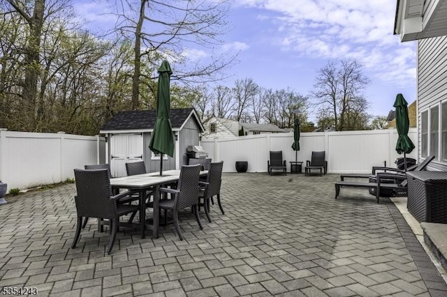 view of patio featuring a fenced backyard, outdoor dining space, an outdoor structure, and a storage shed