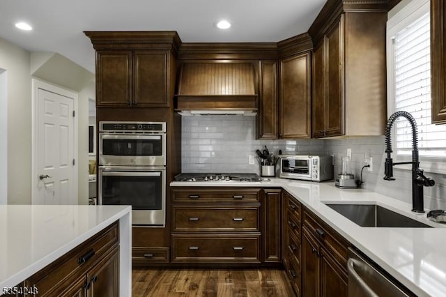 kitchen with a sink, light countertops, stainless steel appliances, custom range hood, and tasteful backsplash