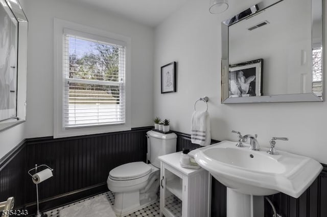 half bathroom with a sink, wainscoting, toilet, and visible vents