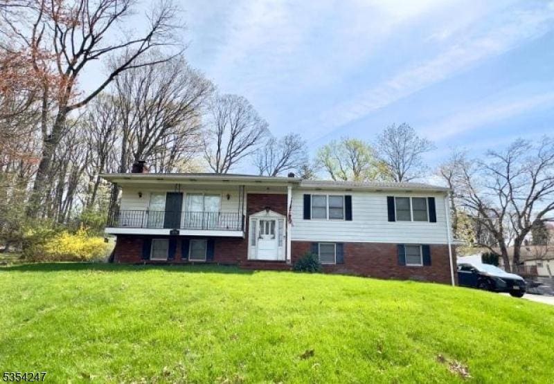 bi-level home featuring brick siding, a chimney, a balcony, and a front lawn