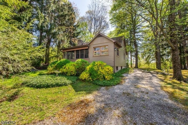 view of side of home featuring driveway, a chimney, and a sunroom