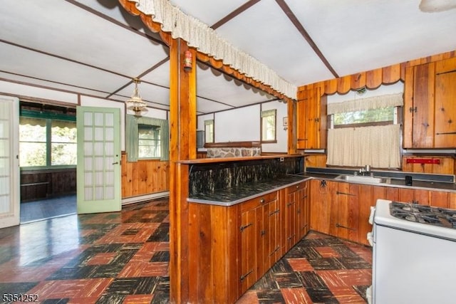 kitchen with brown cabinetry, white gas range oven, dark floors, a sink, and stainless steel countertops