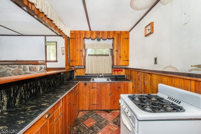 kitchen featuring white gas stove, brown cabinetry, and a wealth of natural light