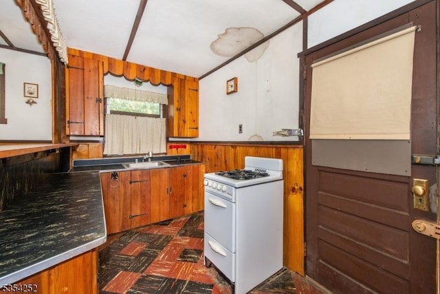 kitchen with brown cabinets, dark floors, white gas range oven, and a sink