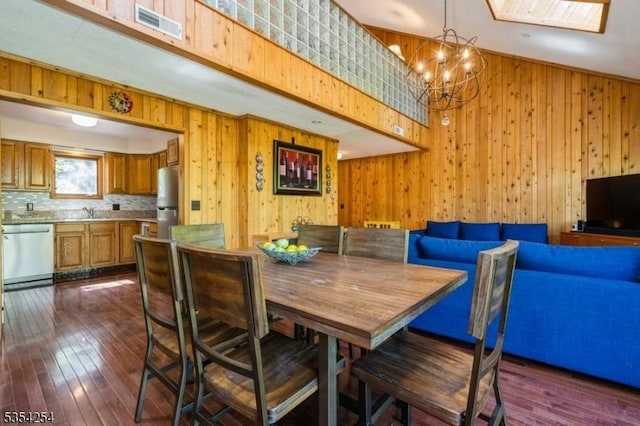 dining room with visible vents, wood walls, an inviting chandelier, dark wood finished floors, and a skylight
