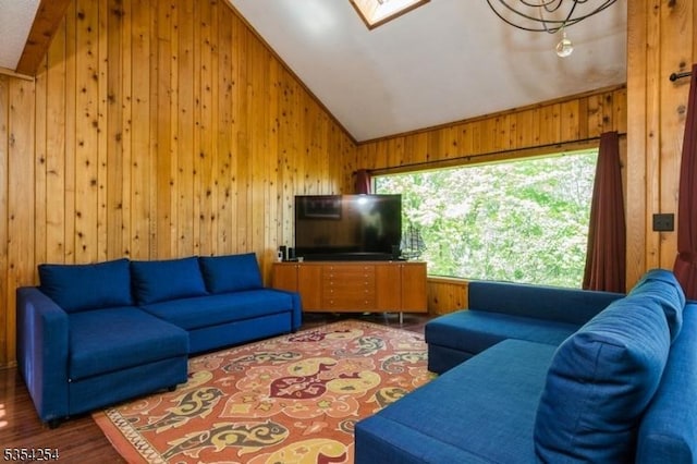 living room featuring wood walls, wood finished floors, and vaulted ceiling with skylight
