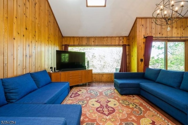 living area with an inviting chandelier, vaulted ceiling, wooden walls, and a wealth of natural light