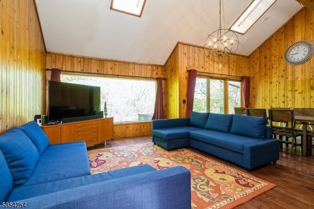 living room featuring wooden walls, a notable chandelier, and vaulted ceiling with skylight