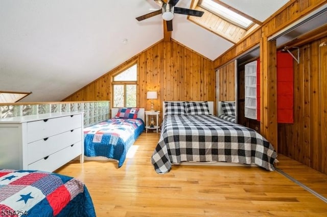 bedroom with wooden walls, ceiling fan, wood finished floors, and vaulted ceiling with skylight