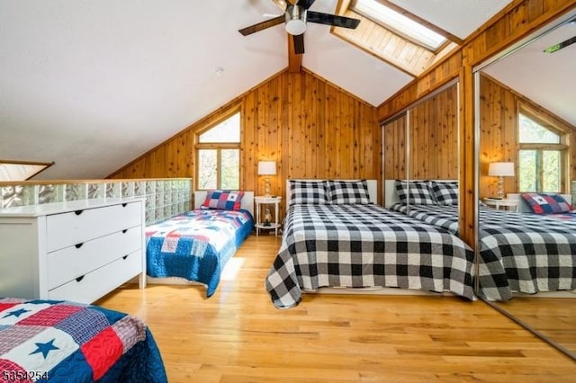 bedroom featuring vaulted ceiling with skylight, multiple windows, wooden walls, and wood finished floors