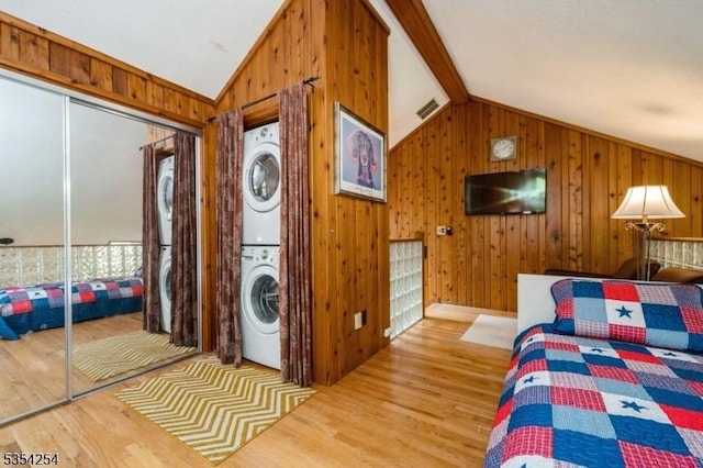 bedroom featuring stacked washing maching and dryer, wooden walls, wood finished floors, and lofted ceiling