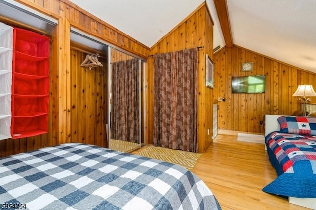 bedroom featuring wood finished floors, wood walls, lofted ceiling, and a closet