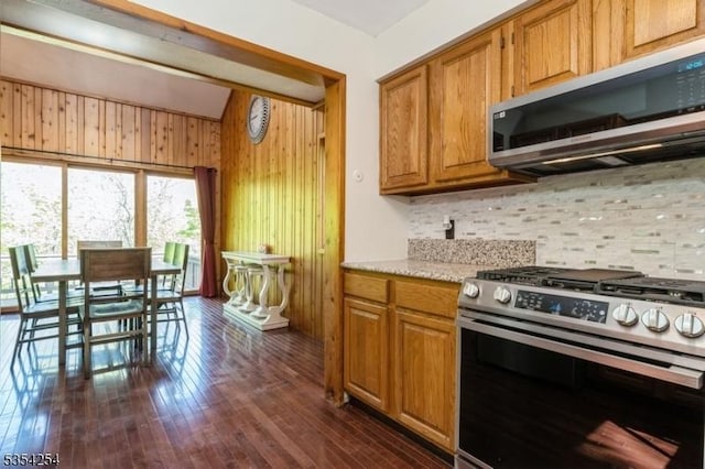 kitchen featuring wooden walls, appliances with stainless steel finishes, decorative backsplash, and dark wood finished floors