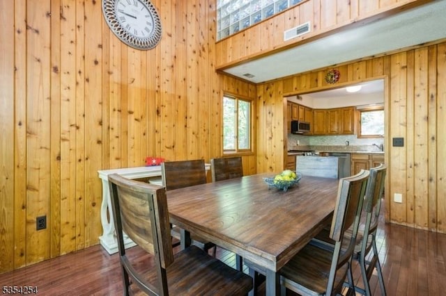 dining space featuring wooden walls, baseboards, visible vents, and dark wood-type flooring