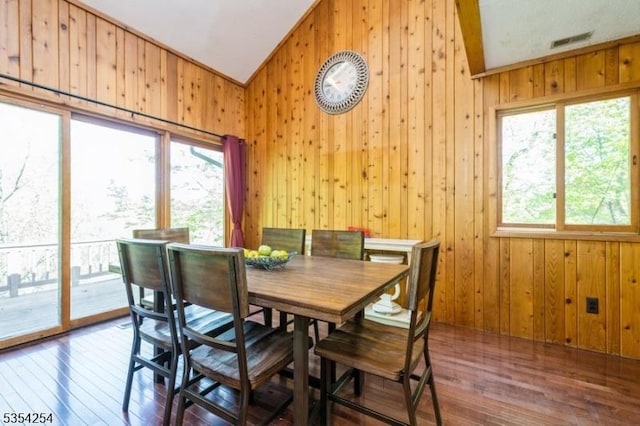 dining space with visible vents, wood walls, vaulted ceiling, and hardwood / wood-style floors