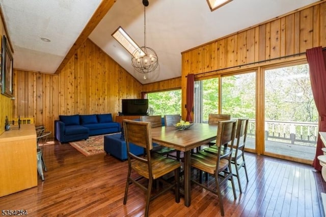 dining space featuring wooden walls, hardwood / wood-style flooring, a notable chandelier, and lofted ceiling