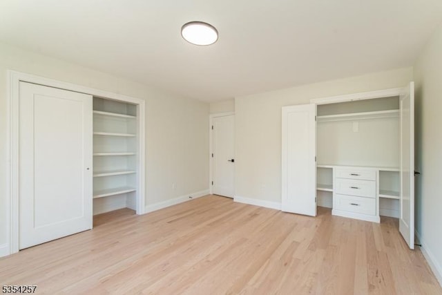 unfurnished bedroom with two closets, baseboards, and light wood-type flooring