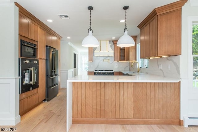 kitchen featuring wall chimney range hood, visible vents, a sink, a baseboard radiator, and black appliances