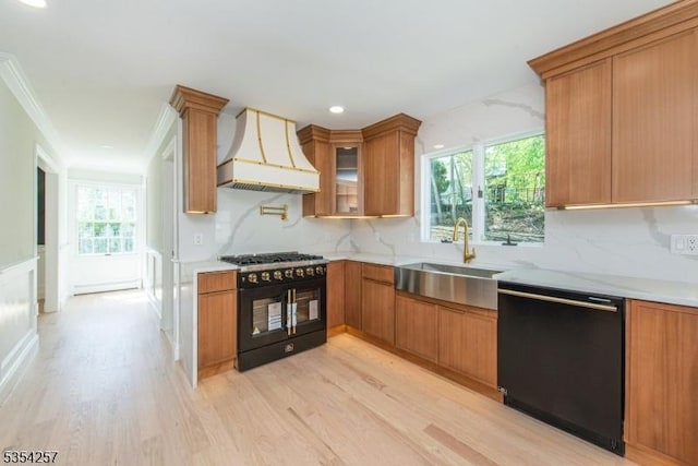 kitchen featuring tasteful backsplash, a sink, premium range hood, black appliances, and light wood-style flooring