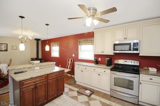 kitchen featuring a wood stove, ceiling fan, a center island, appliances with stainless steel finishes, and decorative light fixtures