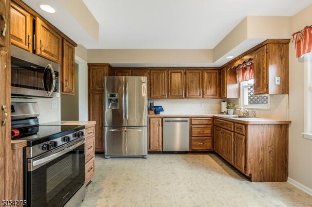 kitchen featuring light countertops, stainless steel appliances, brown cabinetry, and a sink