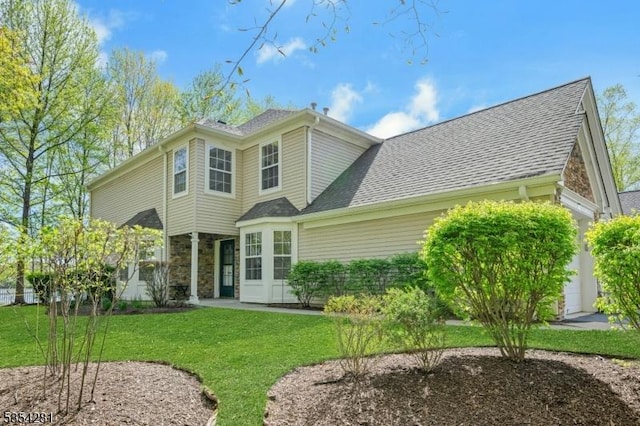 back of house featuring roof with shingles, an attached garage, and a yard