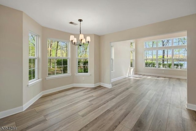 unfurnished dining area featuring baseboards, a chandelier, wood finished floors, and visible vents