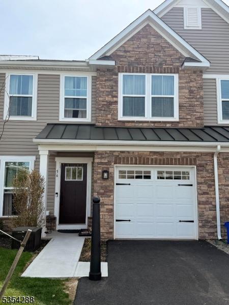 view of property with an attached garage, a standing seam roof, stone siding, and aphalt driveway